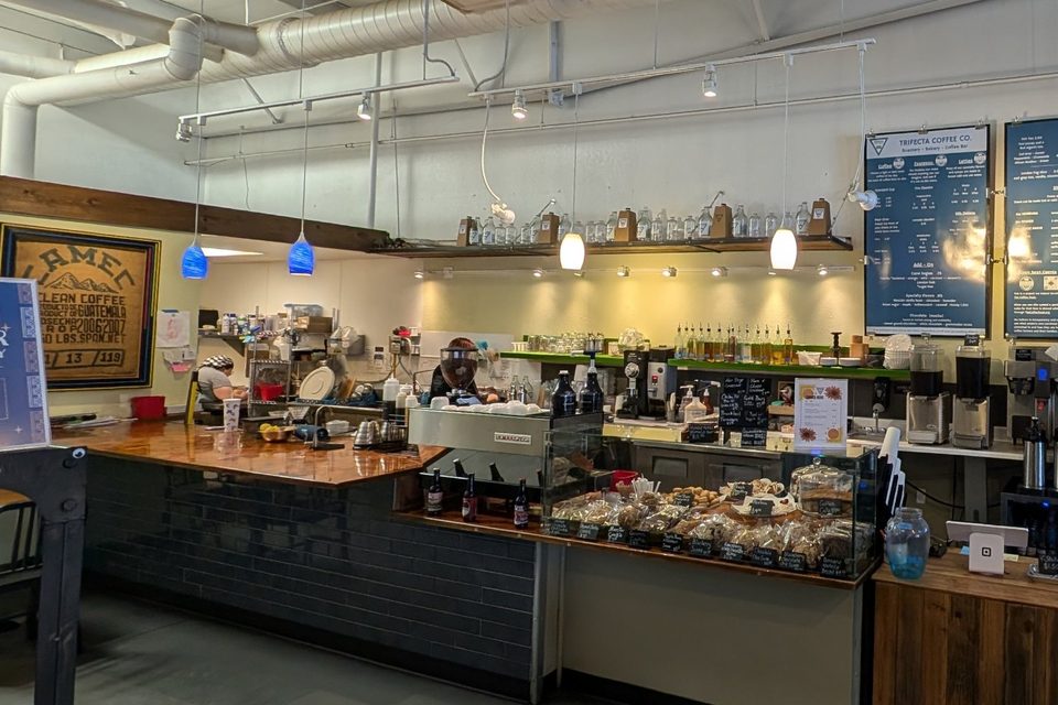 The coffee bar counter with the espresso machine, menu boards and a case of fresh baked goods.