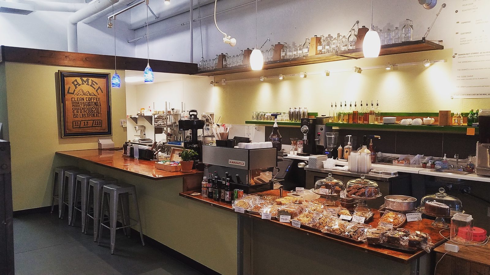 The coffee bar counter with metal stools, the espresso machine and the bakery case.